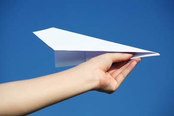 hand holding a paper airplane against a blue sky