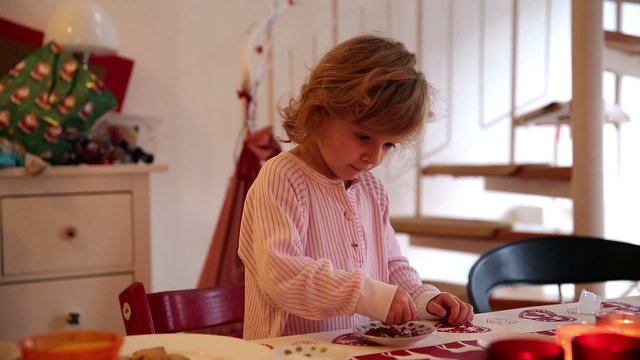 A little girl decorating cookies and treats with icing stars and the help of her mother on advent first