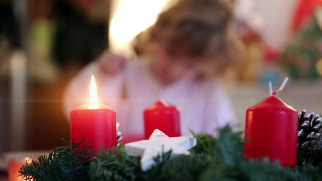Playing with the focus on a burning candle with a little girl nibbling on chocolate topping in the background on advent first