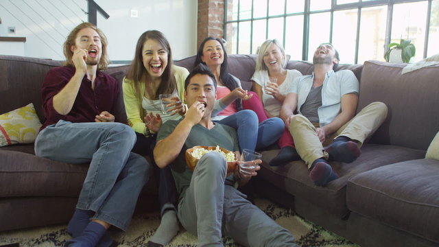 Group of attractive friends sit and eat popcorn whilst watching television.