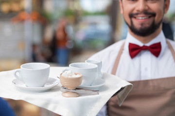 Handsome male cafe worker is serving a client
