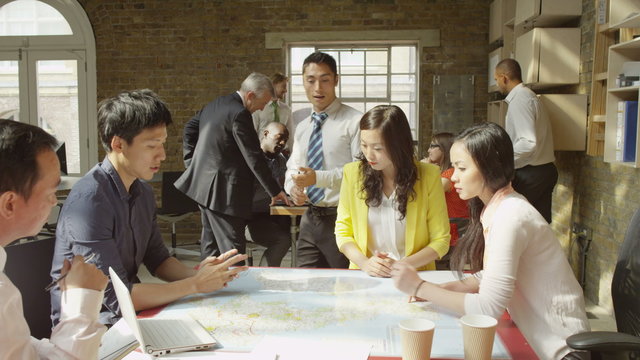  Asian business team in strategy meeting looking at a map of the world