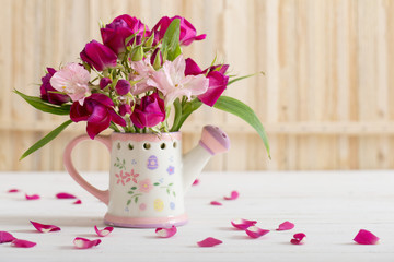 bouquet of bright flowers in watering can on wooden background