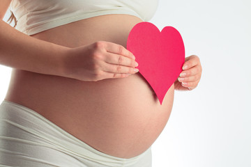 Abdomen of pregnant woman and red heart on white