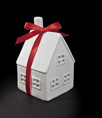 Toy the white house with a red bow on a black background. Dream home