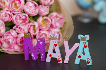 Букет розовых тюльпанов в бумажной обертке и буквы "MAYA" на фоне игрушек