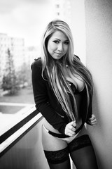 Beautiful blond woman is posing on a balcony. She is wearing a black blazer and underwear. - Mixed race Asian / Caucasian female model. Black and white photography. Glamour and fashion photography.