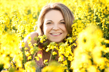 Portrait of beautiful brunette in a yellow rapeseed field,  in Spring. She is wearing a colored sleeveless T-shirt. Fashion photography.