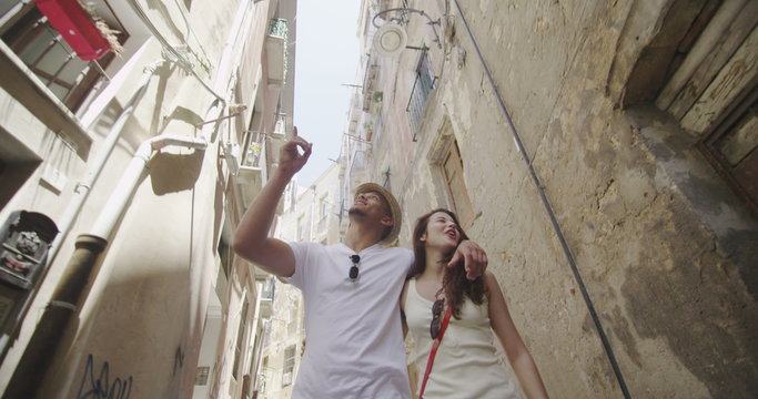 Happy couple on summer vacation walking through narrow city street, looking at the buildings. 