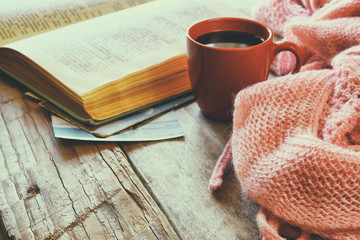 Obraz na płótnie Canvas selective focus photo of pink cozy knitted scarf with to cup of coffee, wool yarn balls and open book on a wooden table 