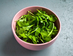 Salad of fresh arugula in a pink bowl on a gray table