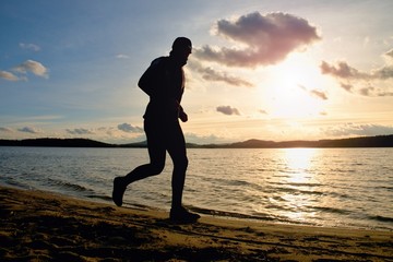 Fototapeta premium Tall man with sunglass and dark cap is running on beach at autumn sunset