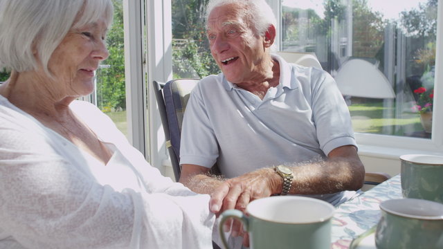 Affectionate senior couple drinking coffee in conservatory on a sunny day