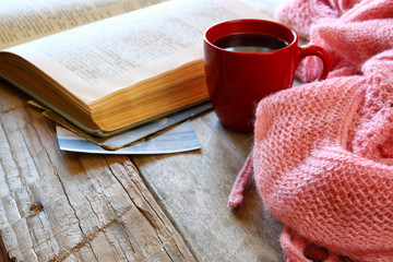 selective focus photo of pink cozy knitted scarf with to cup of coffee, wool yarn balls  and open book on a wooden table

