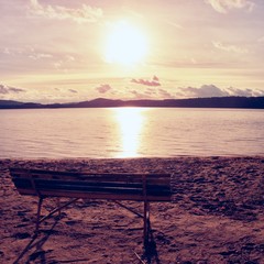 Outdoor empty bench on autumn lake beach. The coast with sunset. Vintage toned photo with lens flare effect