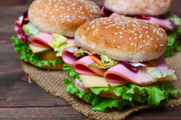 Burger sandwich with sausage, cheese and vegetables on a wooden background