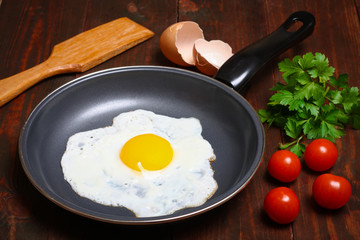 Pan of fried eggs, with cherry-tomatoes and parsley on a wooden table surface
