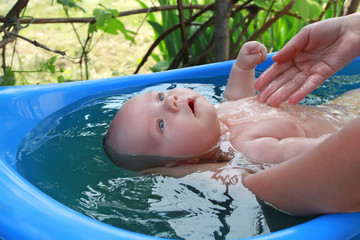 Mum bathes baby in a blue bath. Bathing the baby in the vineyard