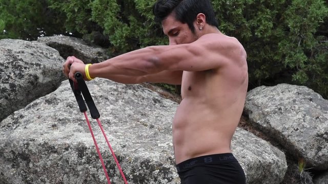 A bodybuilder exercising with a resistance rope in the mountains
