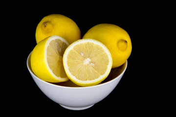 Whole and Cut Lemons in White Bowl on Black Background
