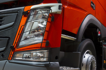 Headlight of oversize truck with stars, orange bodywork, bumper, hood, fender, door and wheel with...
