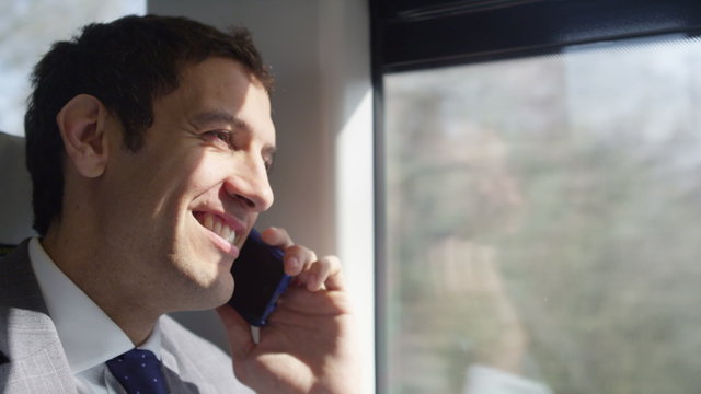  Attractive smiling businessman making mobile phone call on train journey.