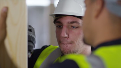  Male construction worker or tradesman working with male apprentice, showing him how to use a drill. 