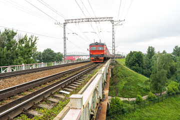 Naklejka premium Red and grey suburban electric train moves towards on railroad turn vanishing against skyline background. Moscow, Russia. 