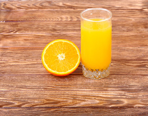 Glass of freshly pressed orange juice with sliced orange half on wooden table