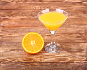 Glass of freshly pressed orange juice with sliced orange half on wooden table