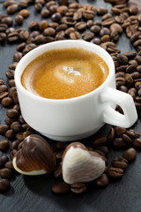 cup of espresso, coffee beans background and chocolate candies 