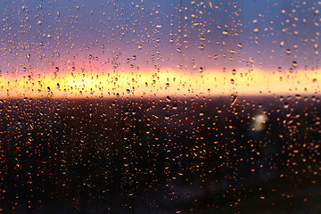 Fototapeta na wymiar Water drops on a window glass after the rain. The sky with clouds and sun on background.