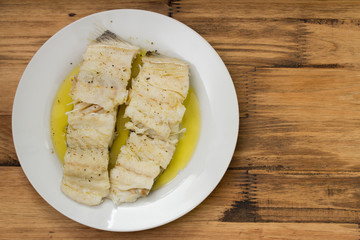 boiled cod fish with olive oil on white plate on brown wooden background