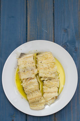 boiled cod fish with olive oil on white plate on blue wooden background