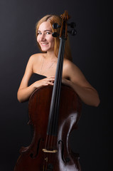 Beautiful girl with a cello on a black background. Cellist. Girl musician.
