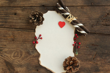Empty sheet for text and heart, pine cone and chocolate roll around it on wooden table background