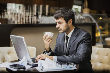 Fototapeta na wymiar мужчина в деловом костюме с вдохновением работает на ноутбуке, в его руке чашка кофе