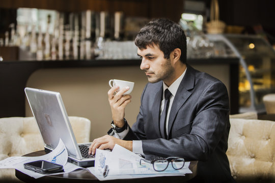 мужчина в деловом костюме с вдохновением работает на ноутбуке, в его руке чашка кофе