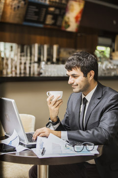 мужчина в деловом костюме с вдохновением работает на ноутбуке, в его руке чашка кофе