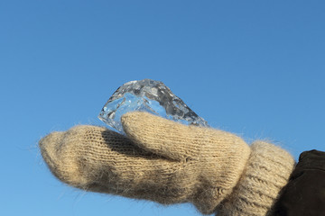 Ice crystal in the female hands dressed in woolen mittens against the blue sky