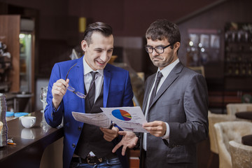 Два бизнесмена в кафе изучают документы и отчеты и удивляются результатам