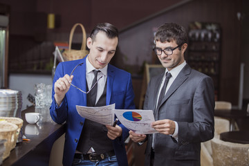 Два топ-менеджера в деловых костюмах в кафе вместе изучают документы и графики