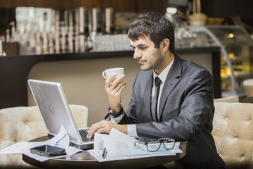Fototapeta na wymiar Молодой бизнесмен в кафе увлеченно читает новости в ноутбуке и радуется