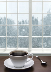 A cup of coffee and snowstorm view from the window on the background