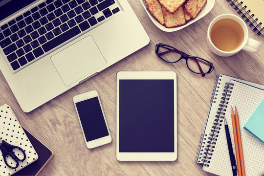 Laptop, smartphone, tablet and tea cup on wooden table