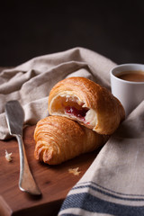 Closeup of croissant with jam and coffee on a wooden background.