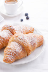 Couple of croissants on a white plate with coffee and berries.
