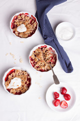 Crumble with oatmeal, wholemeal and strawberry in white bowls on a white table. Top view.