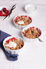 Crumble with oatmeal, wholemeal and strawberry in white bowls on a white table.