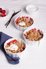 Crumble with oatmeal, wholemeal and strawberry in white bowls on a white table..
